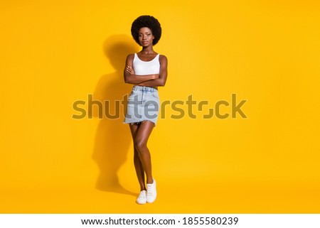 Photo of lovely cool black young girl crossed hands wear white singlet jeans mini skirt sneakers isolated yellow color background