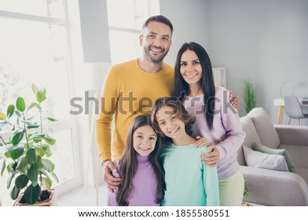 Photo of full family four members two little children embrace shiny smile wear colorful pullover in living room indoors