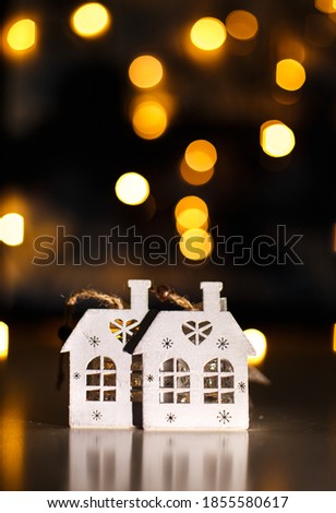 The picture shows wooden Christmas tree decorations: two houses. In the background there is a bokeh from a yellow garland. Image with a selective focus