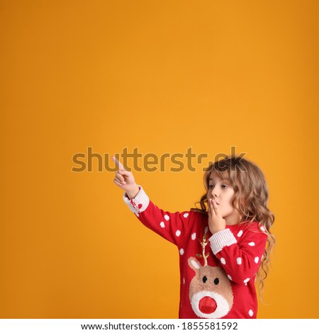 Cute little girl in red Christmas sweater against orange background. Space for text