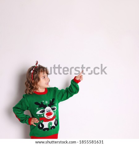 Cute little girl in green Christmas sweater pointing against white background
