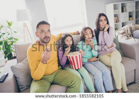 Photo of full family four people sit sofa eat popcorn watch movie scared wear colorful pullover in living room indoors