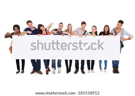 Full length portrait of confident multiethnic college students displaying blank billboard against white background