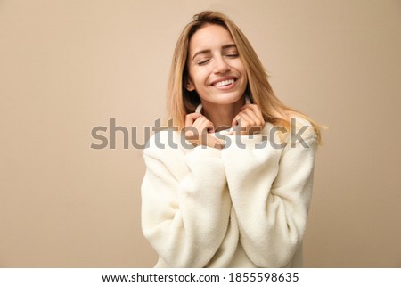 Beautiful young woman wearing knitted sweater on beige background