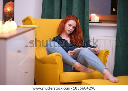 Relaxed happy woman reading a book sitting on a couch at home