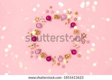 Wreath made of Christmas decorations and gold confetti. Minimalist festive frame on a pink pastel background.