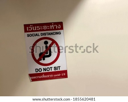 Social Distancing and Do not Sit Sign on the wall. The Thai Text is “Social Distancing” and “Reduce risk from Covid-19”