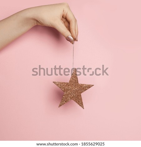 Christmas card with gold star in woman hand on pink background