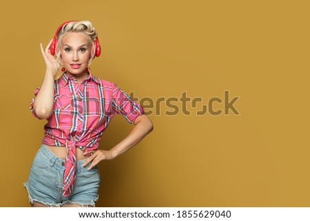 Pin-up woman fashion model with headphones listening music on bright yellow banner background with copy space