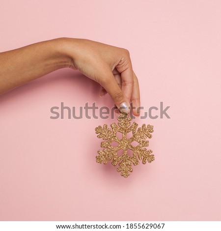 Gold snowflake in female hand on pink background. Christmas holiday concept