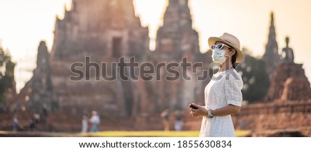Happy tourist woman wearing surgical face mask and taking Photo by mobile smartphone, protection COVID-19 pandemic during visiting in Ayutthaya temple. new normal, safety travel and travel concept