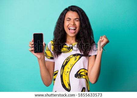 Photo of pretty excited lady hold telephone screen empty space closed eyes wear banana print t-shirt isolated teal color background