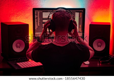 Musician working in a modern home music studio equipped in the professional coputer, dj deck, midi controller and big audio speakers. Royalty-Free Stock Photo #1855647430