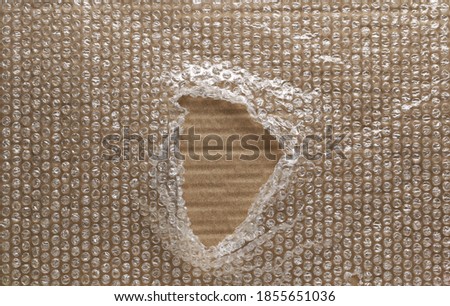 Blank cardboard covered with torn bubble wrap that has hole in middle background and texture Royalty-Free Stock Photo #1855651036