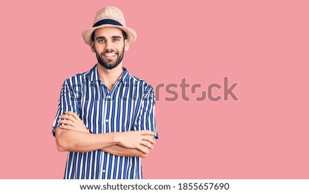 Young handsome man with beard wearing summer hat and striped shirt happy face smiling with crossed arms looking at the camera. positive person. 
