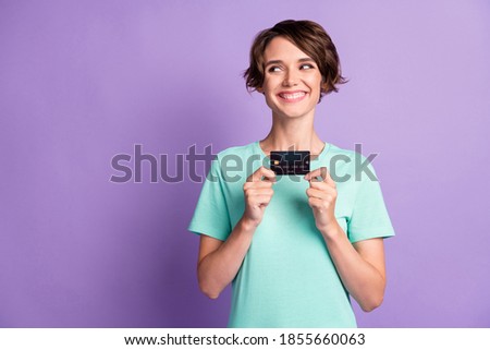 Photo of shiny young woman dressed casual turquoise clothes holding card looking empty space isolated violet color background