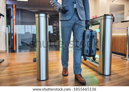 Waist-down photo of a man with carry-on crossing the electronic gate at the airport lounge