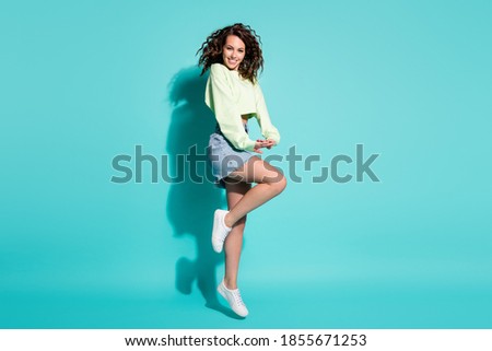 Full length body size photo of pretty flirty coquettish girl jumping high smiling laughing isolated on vibrant teal color background