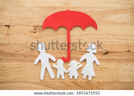 Life insurance concept. Paper cutout of family (father, mother, son and daughter) under red umbrella on wooden background. Insurance is life planning for happy future.