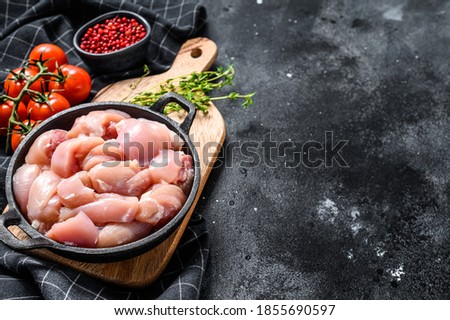 Sliced chicken thighs fillet without skin in a pan. Black background. Top view. Copy space