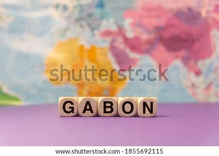 The word Gabon written with wooden dices in front of a purple background and a geographic map