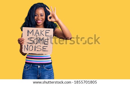 Beautiful african american woman holding make some noise banner doing ok sign with fingers, smiling friendly gesturing excellent symbol 