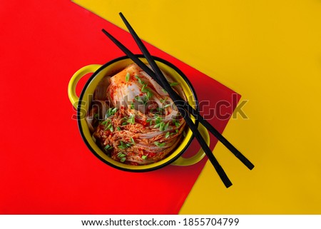 Kimchi cabbage in a bowl with chopsticks on a colored background, top view, Korean cuisine. Trend food photography