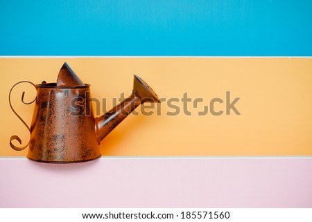 old and rusty watering can with colorful wood background