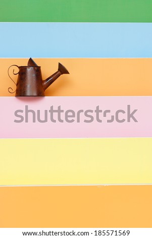 old and rusty watering can with colorful wood background