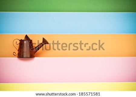 old and rusty watering can with colorful wood background 