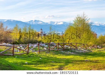 Bansko, Bulgaria spring landscape with the wooden fence, trees, tower of chalet and snowy Rila mountains peaks Royalty-Free Stock Photo #1855723111