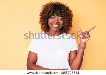 Young african american woman wearing casual white t shirt smiling cheerful pointing with hand and finger up to the side 