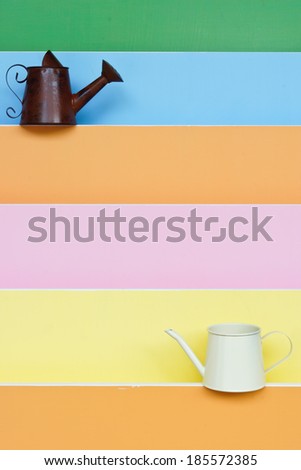 old and and new watering can with colorful wood background