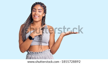 Young african american woman with braids wearing sportswear amazed and smiling to the camera while presenting with hand and pointing with finger. 