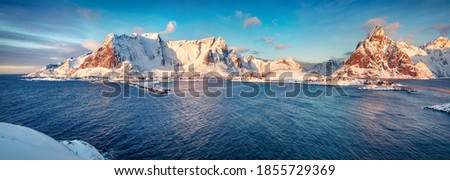 Panoramic morning cityscape of Reine town. Gorgeous view of Lofoten Island with Reinebringen peak on background. Cold winter scene of Norwegian sea. Landscape photography.
