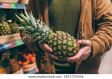 A male shopper in a supermarket holds pineapples in his hands