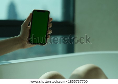 close up hand showing green screen smart phone while in the bathtub at home