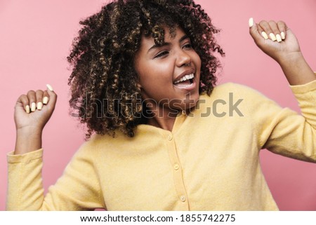 Happy african american woman dancing and laughing at camera isolated over pink wall