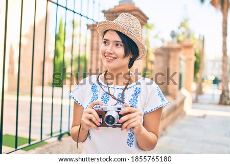 Young latin tourist girl on vacation smiling happy using vintage camera at the city.