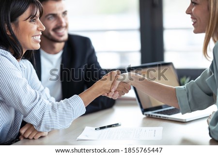 Shot of attractive real-estate agent shaking hands with young couple after signing agreement contract in the office.