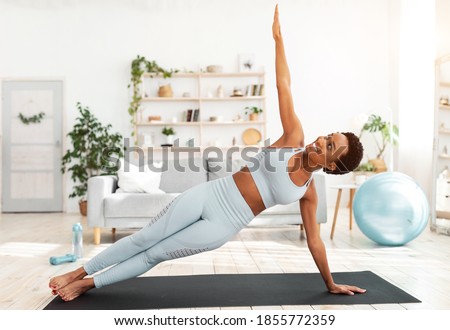 Attractive fit black lady standing in side plank on sports mat at home. Motivated African American woman doing strength exercises, aerobics or yoga. Healthy lifestyle concept Royalty-Free Stock Photo #1855772359
