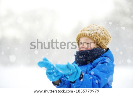 Little boy having fun playing with fresh snow during snowfall. Baby catching snowflakes on gloves. Kid dressed in warm clothes, hat, hand gloves and scarf. Active winter outdoors leisure for child