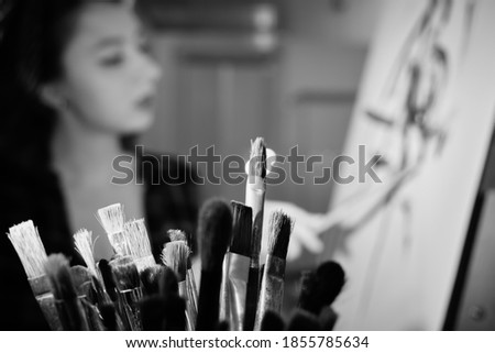 young pretty woman artist with brush near easel draw picture, defocused image, monochrome