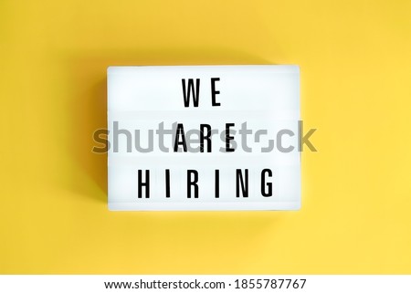 Lightbox with a words text We Are Hiring board on yellow background.  Surviving economical and financial crisis. Job seeking, recruiting and business concept.