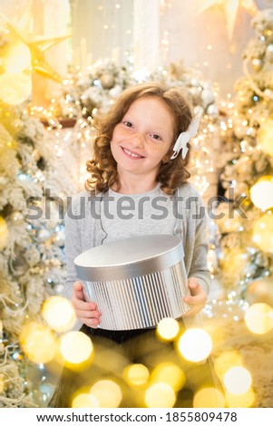 red-haired girl opens a gift near the Christmas tree. smiles, garland, lights, festive atmosphere, new year