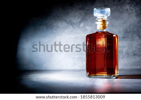 square shaped whiskey bottle in rays of light on dark gray cement background