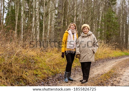 Senior woman and mature woman are walking in the autumn forest by the forest dirt road. 