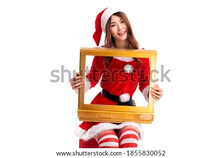 Young woman in santa claus costume holding a golden TV frame sitting on a wooden box isolated on white background.