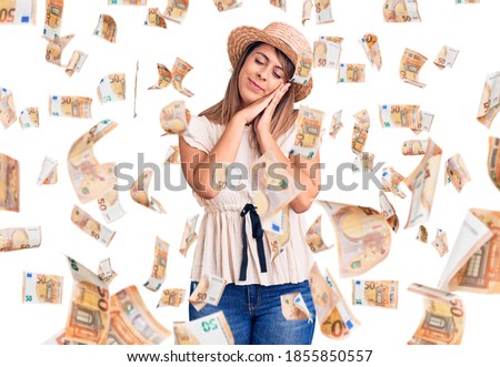 Young beautiful woman wearing summer hat and t-shirt sleeping tired dreaming and posing with hands together while smiling with closed eyes.