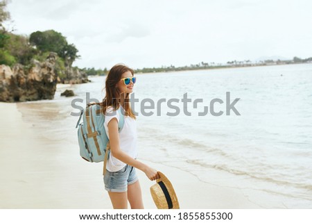 Traveler with a backpack on her back walks along the seashore on the beach and glasses on her face